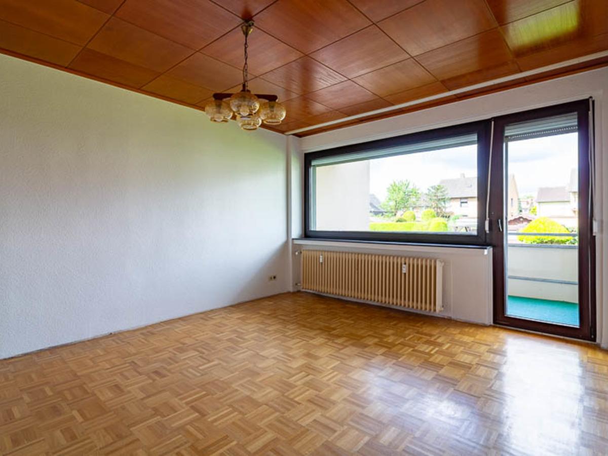 Das Wohnzimmer mit Parkettboden und Zugang zum Balkon lädt zum Wohlfühlen ein