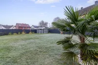 Weitläufiger Garten mit gepflegtem Rasen, Palmen und einem Gartenhaus.