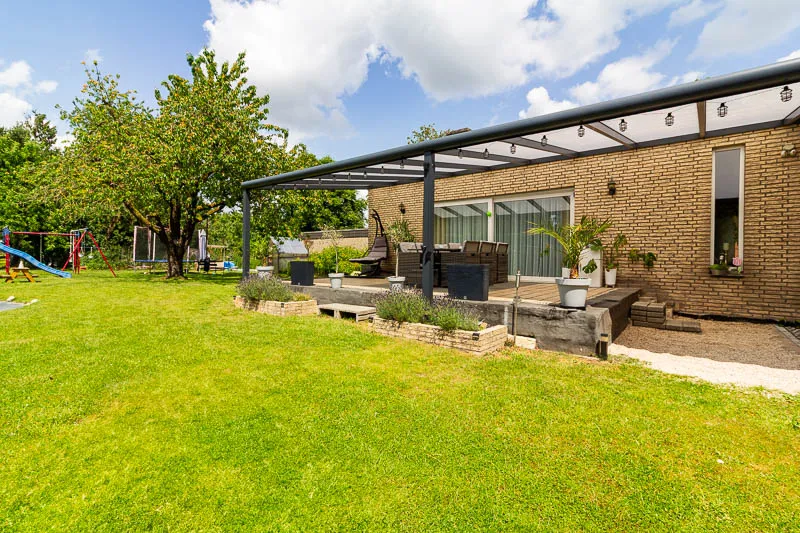 Weitläufiger Garten mit gepflegtem Rasen, Spielbereich und hochwertiger Terrassenüberdachung.